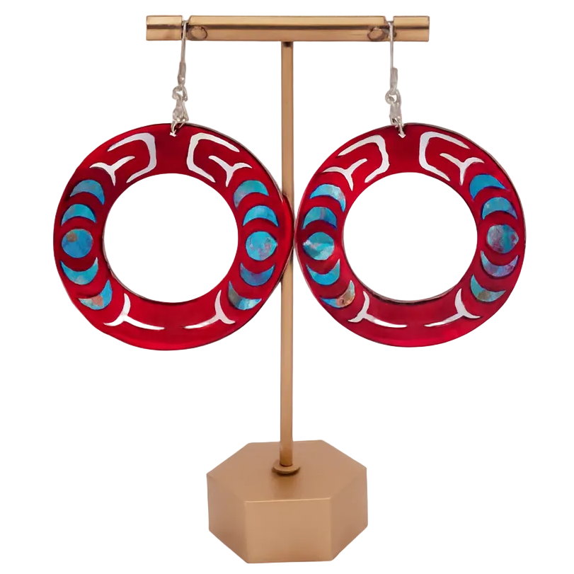 Red hoop earrings with blue and gray patterns on a gold stand against a white background