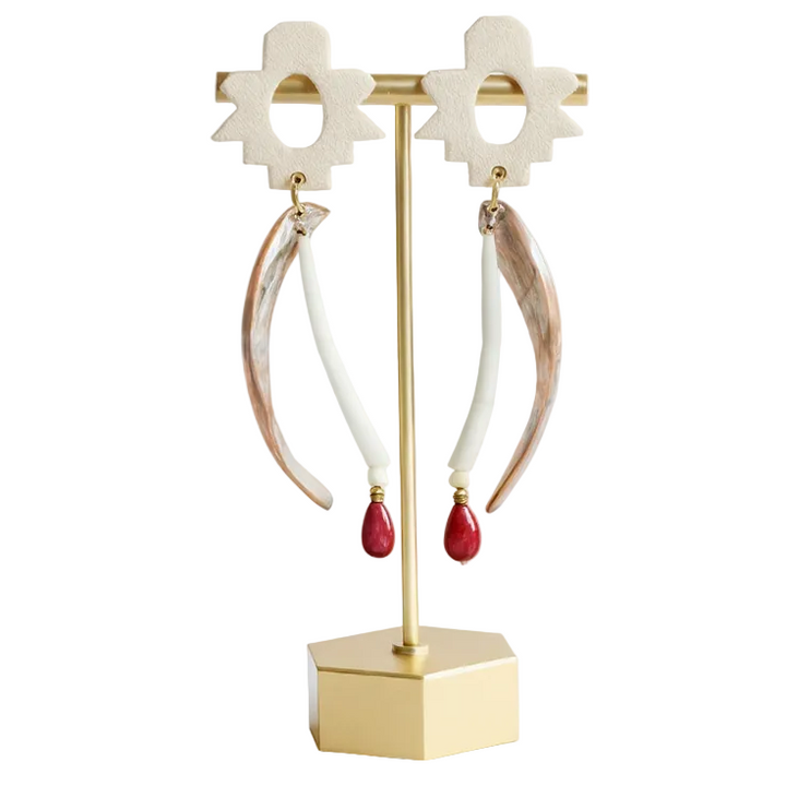 Pair of hoop earrings with red drops on a gold earring stand against a white background