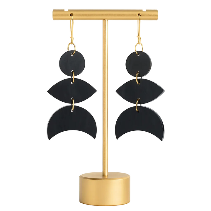 Black layered earrings on a gold stand against a white background